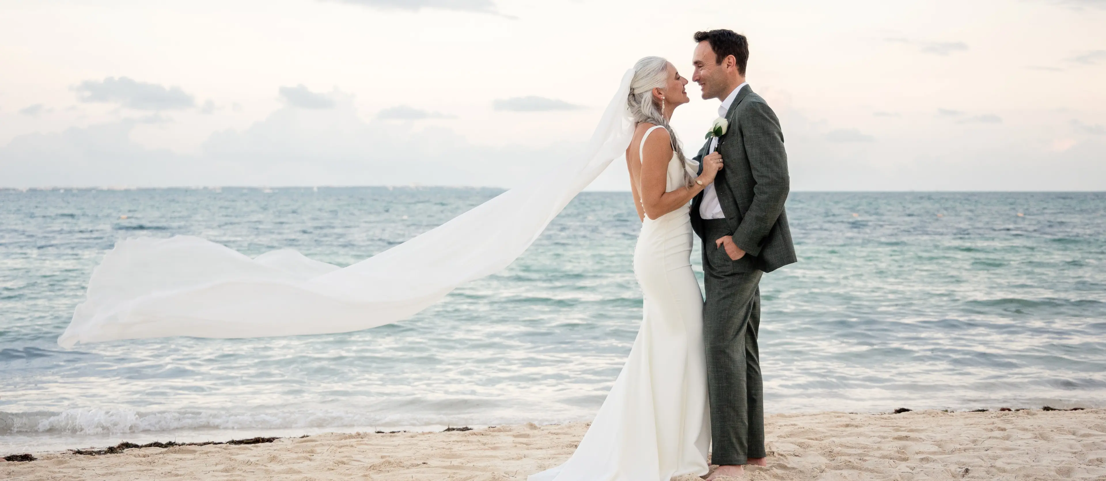 Lindsey & Jeff portrait on the beach with a long veil blowing in the wind at Garza Blanca Cancun