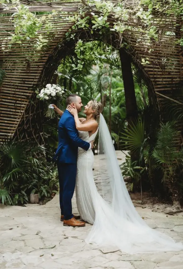 Samantha & William leaning in for a kiss under a tropical wooden archway at Secrets Moxche, Playa Del Carmen