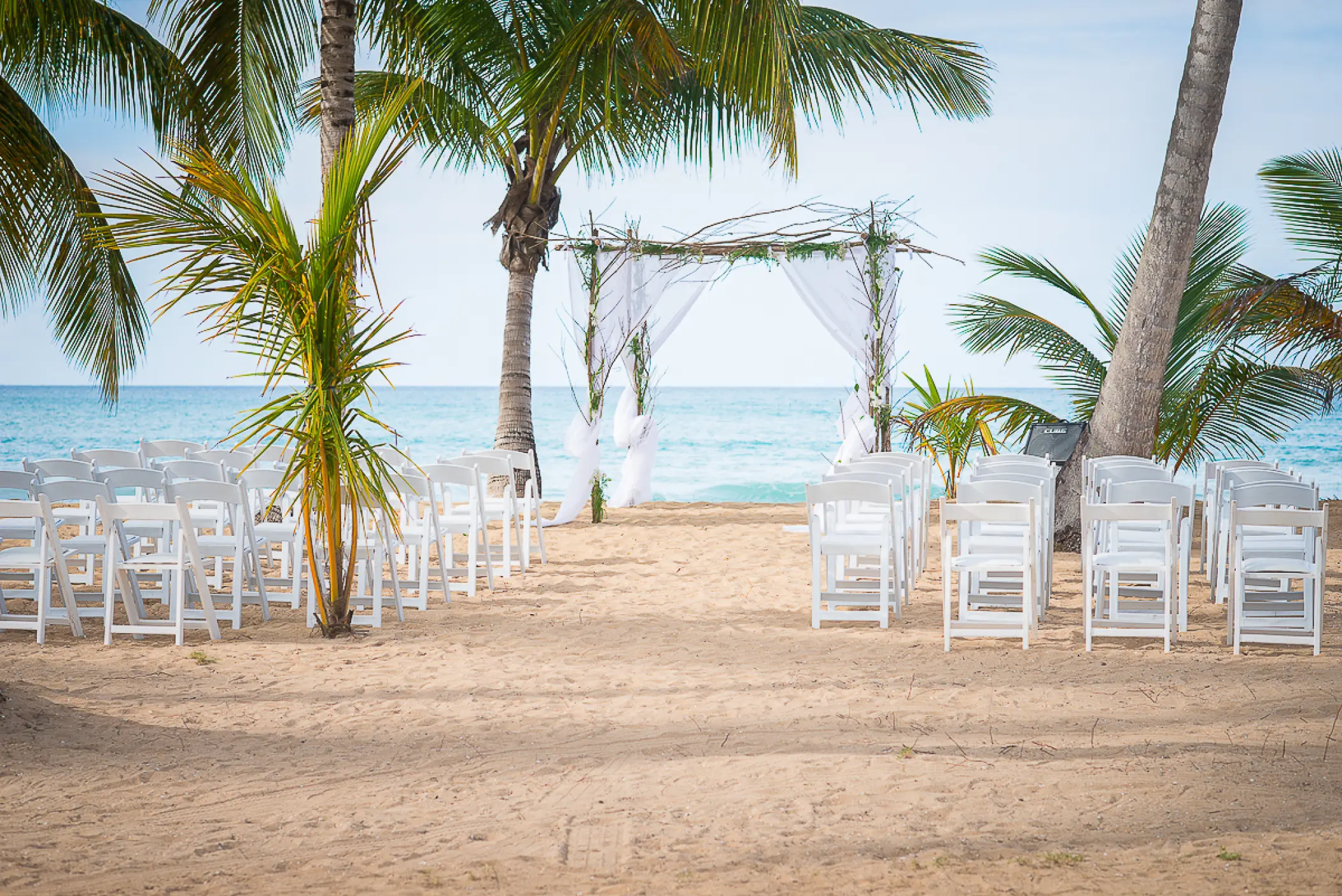 Beachfront wedding ceremony with a white arch and wooden chairs at Sublime Samaná, Samana