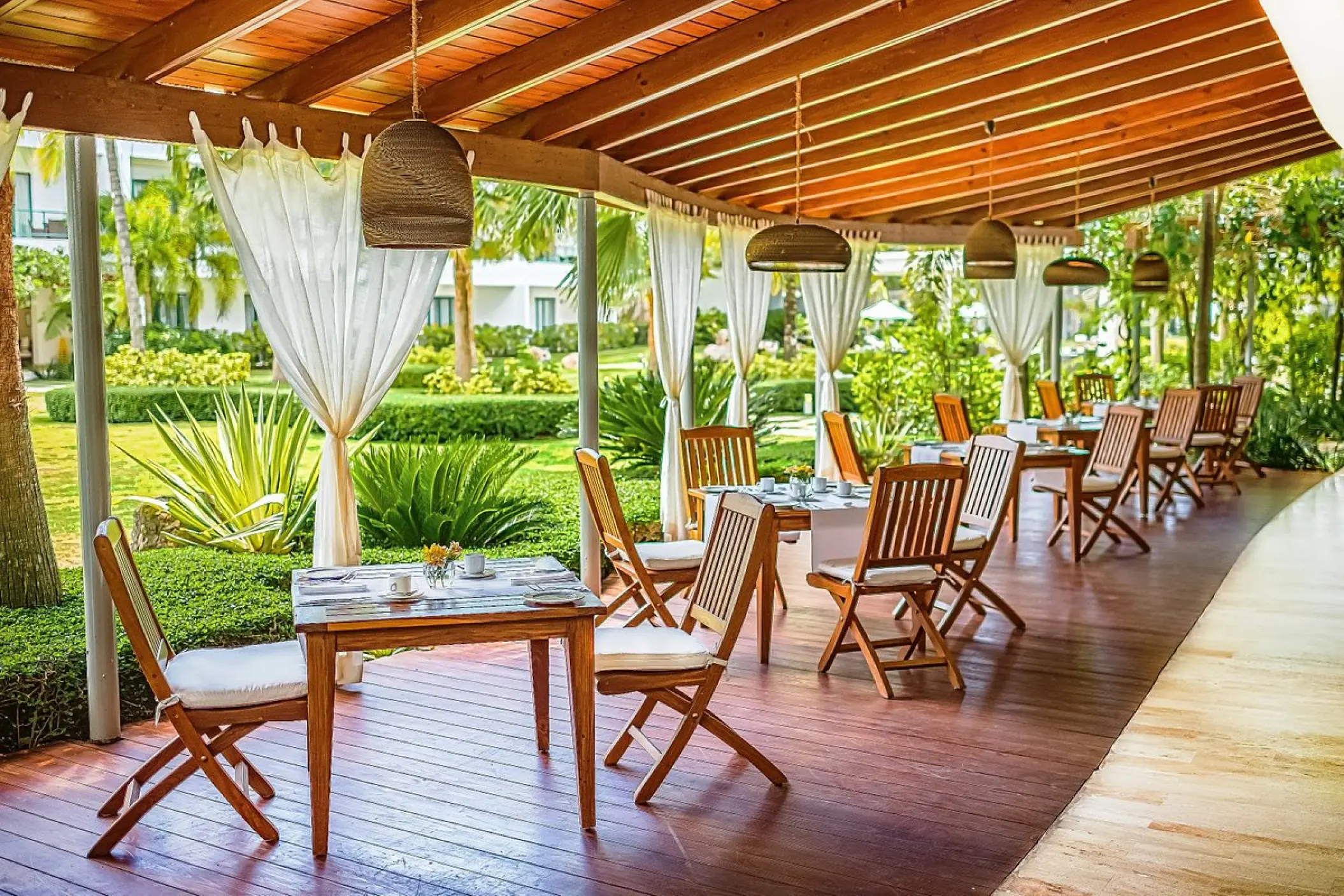 Outdoor terrace restaurant with wooden tables and woven pendant lights at Sublime Samana, Samana
