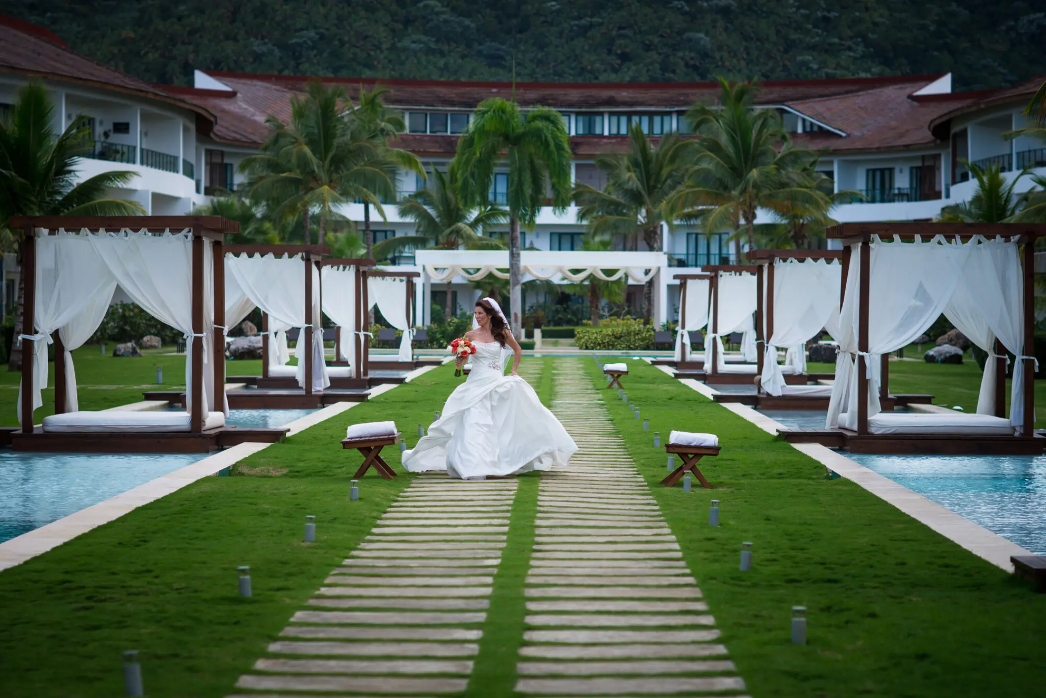 Bride walking on a wooden path between cabanas and pools at Sublime Samana, Samana