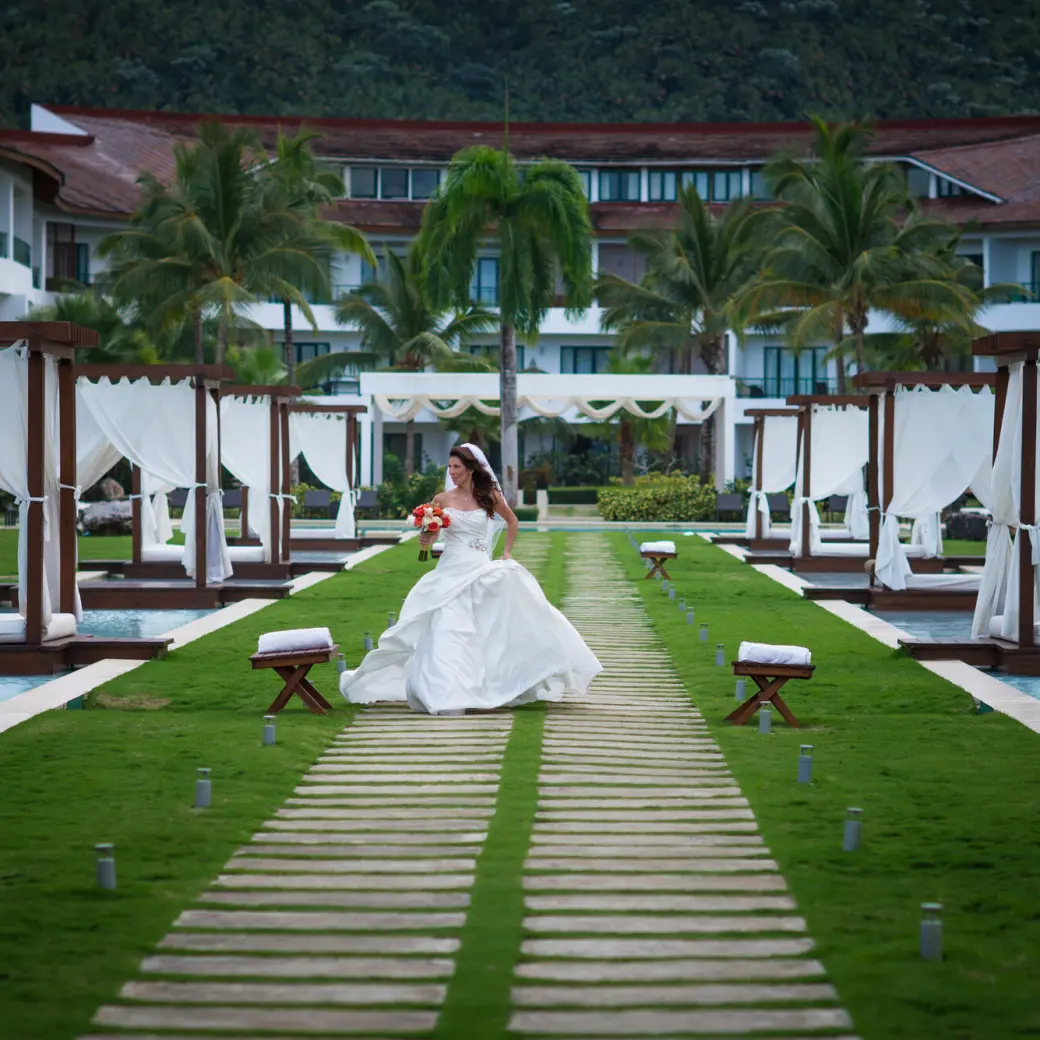 Bride walking on a wooden path between cabanas and pools at Sublime Samana, Samana