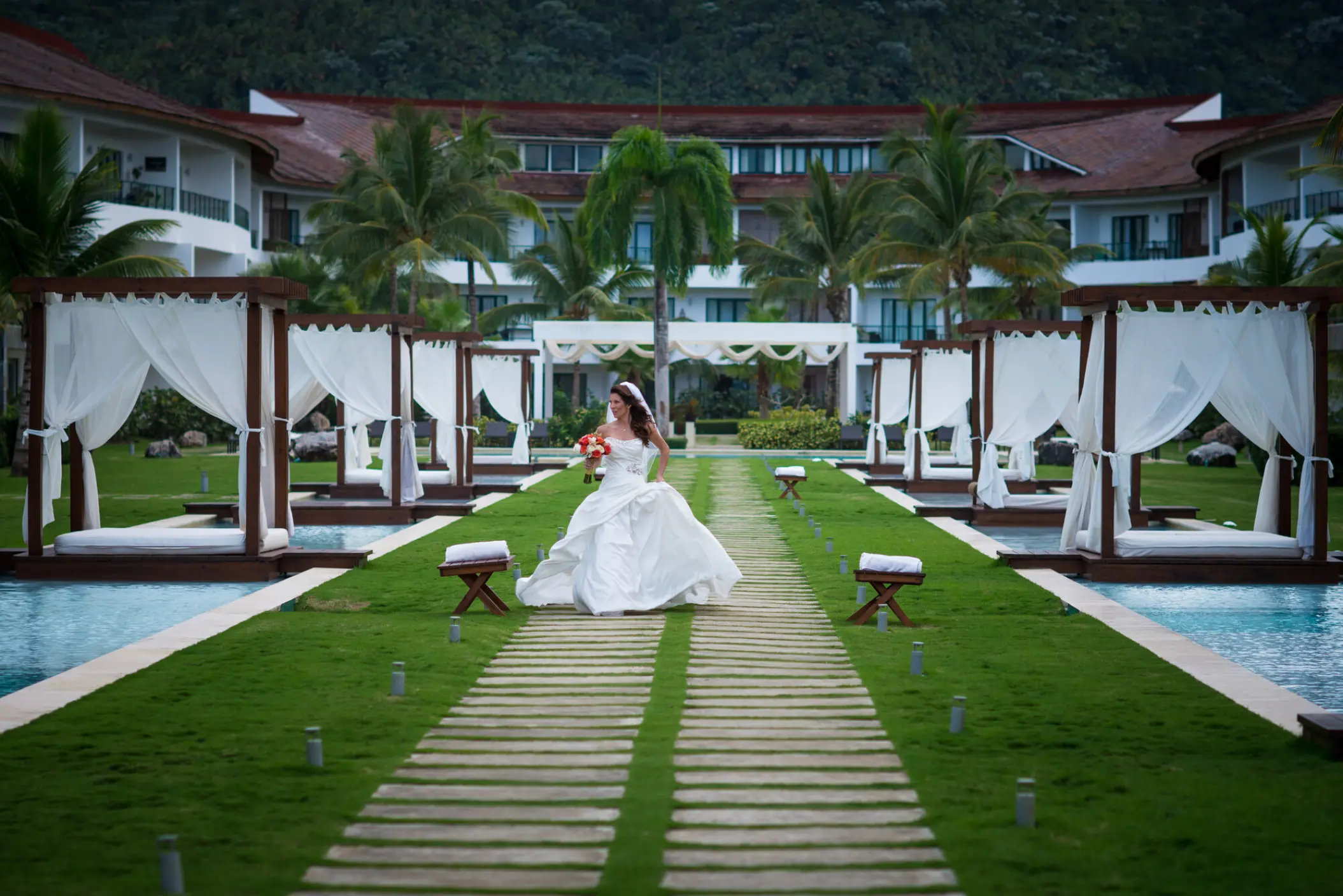 Bride walking on a wooden path between cabanas and pools at Sublime Samana, Samana