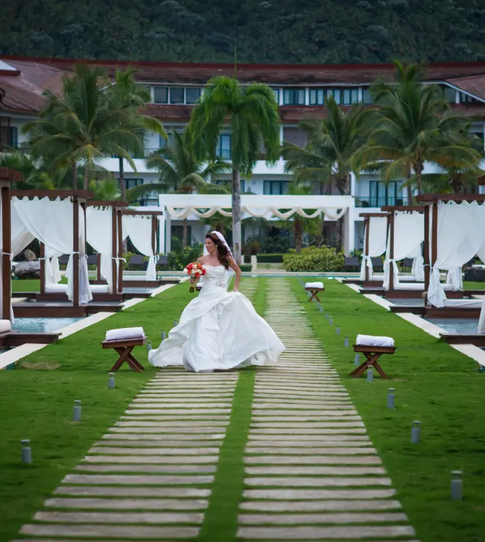 Bride walking on a wooden path between cabanas and pools at Sublime Samana, Samana