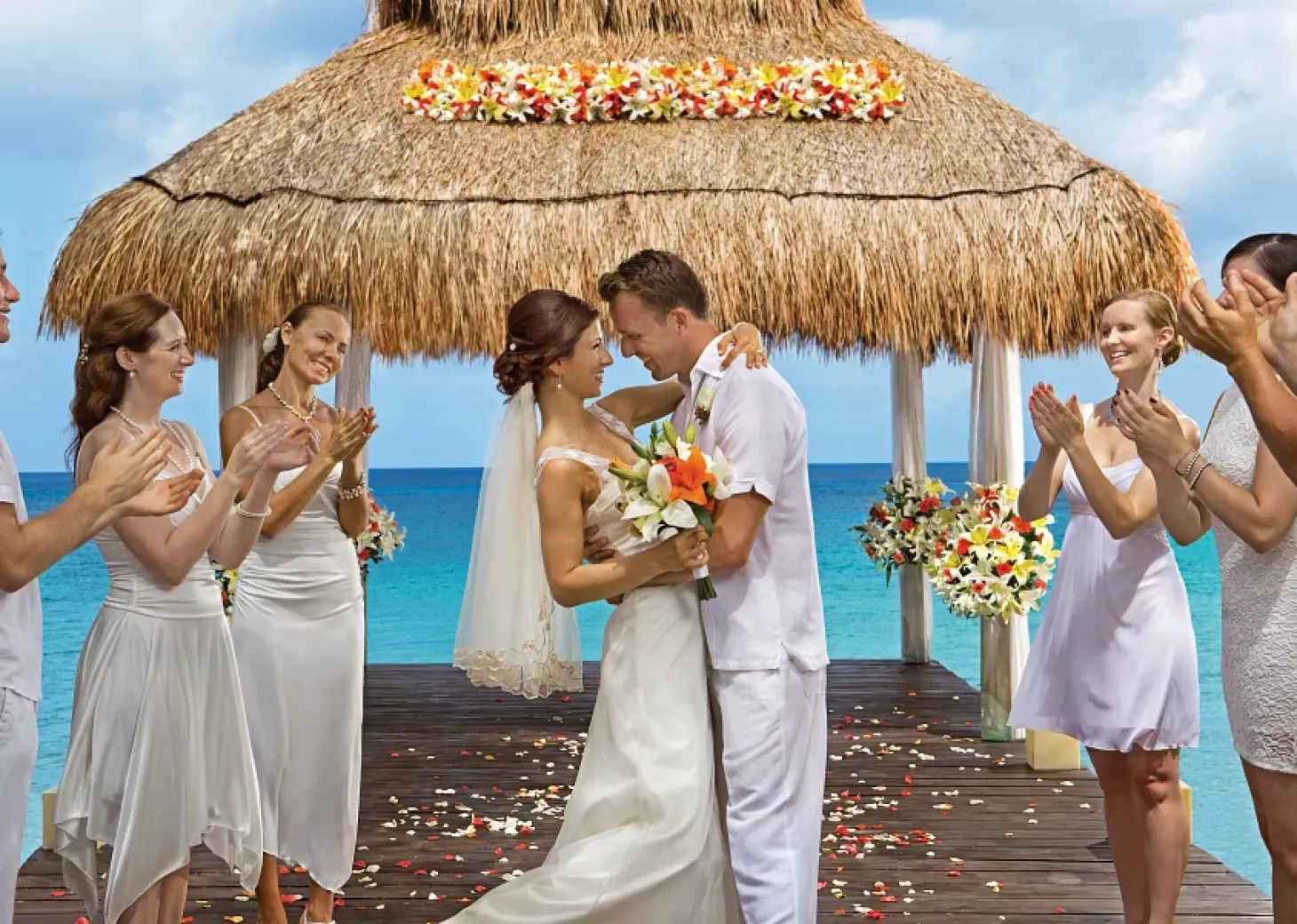 Bride and groom embrace under a thatched gazebo during a beach ceremony at Sunscape Akumal, Tulum
