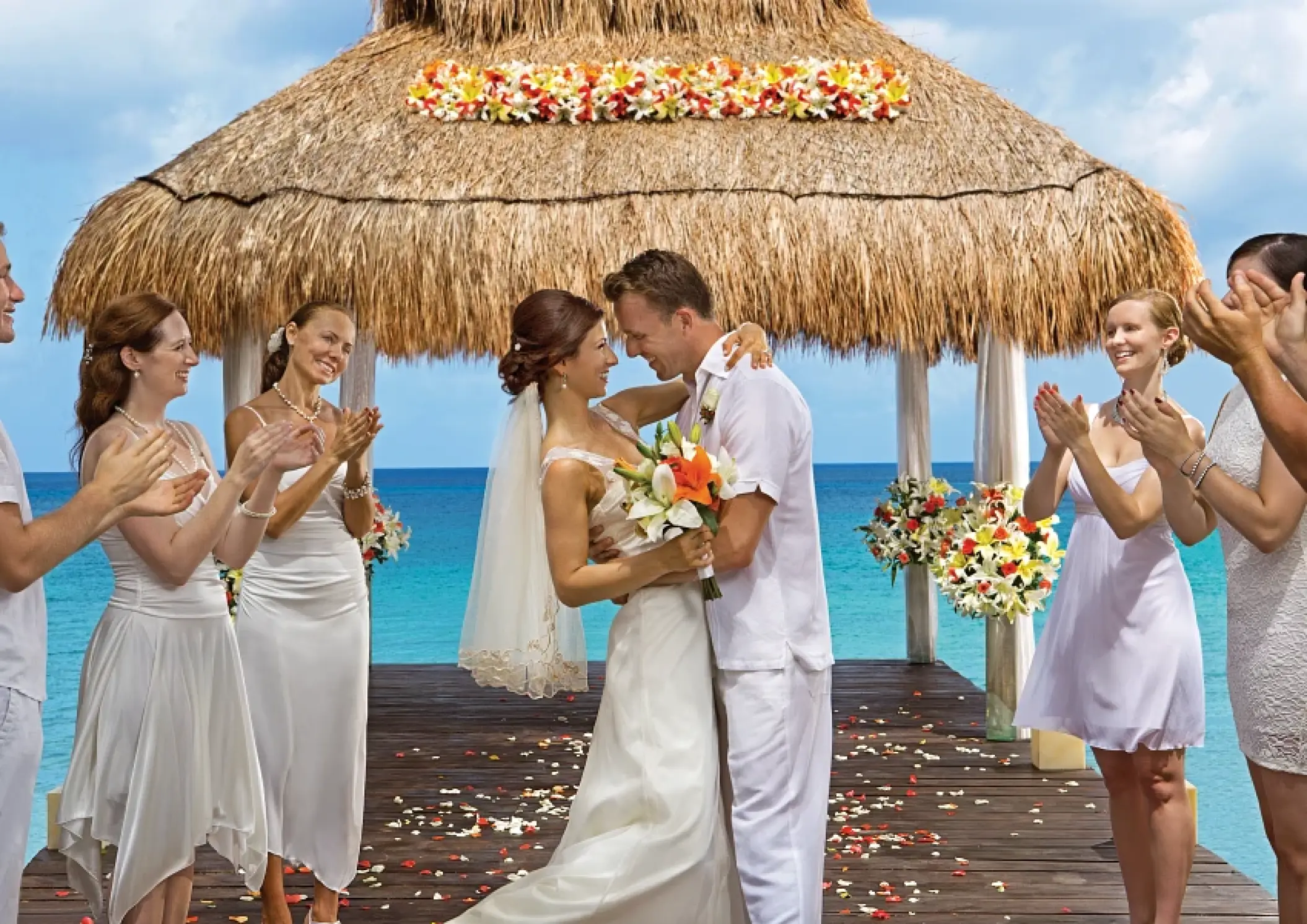 Bride and groom embrace under a thatched gazebo during a beach ceremony at Sunscape Akumal, Tulum
