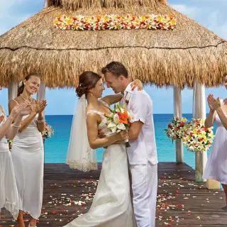 Bride and groom embrace under a thatched gazebo during a beach ceremony at Sunscape Akumal, Tulum