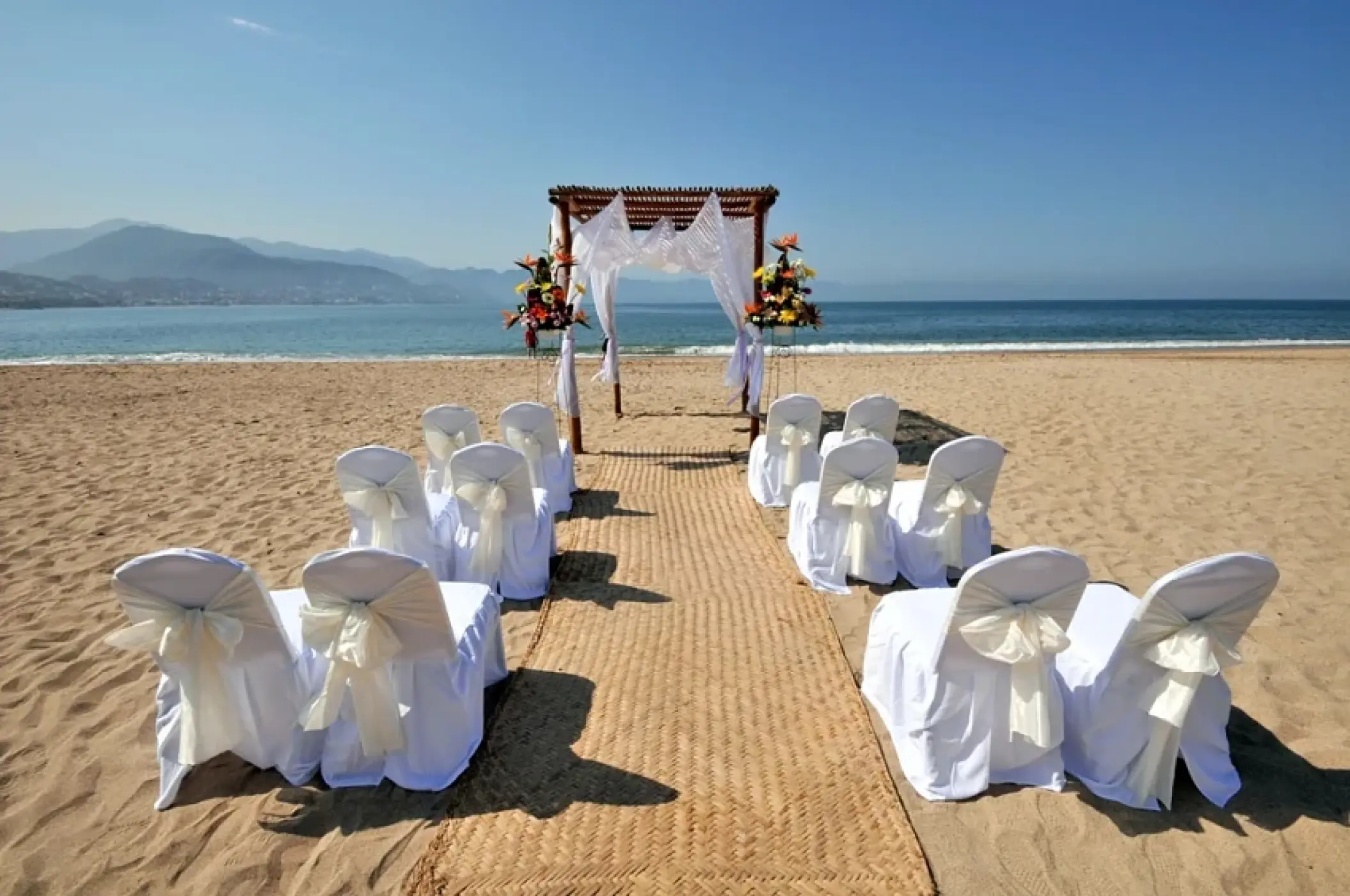 Beachfront wedding ceremony setup with white chair covers and a floral arch at Sunscape Akumal Beach, Tulum