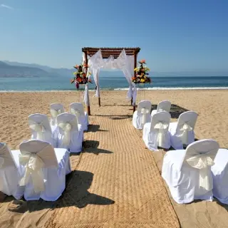 Beachfront wedding ceremony setup with white chair covers and a floral arch at Sunscape Akumal Beach, Tulum