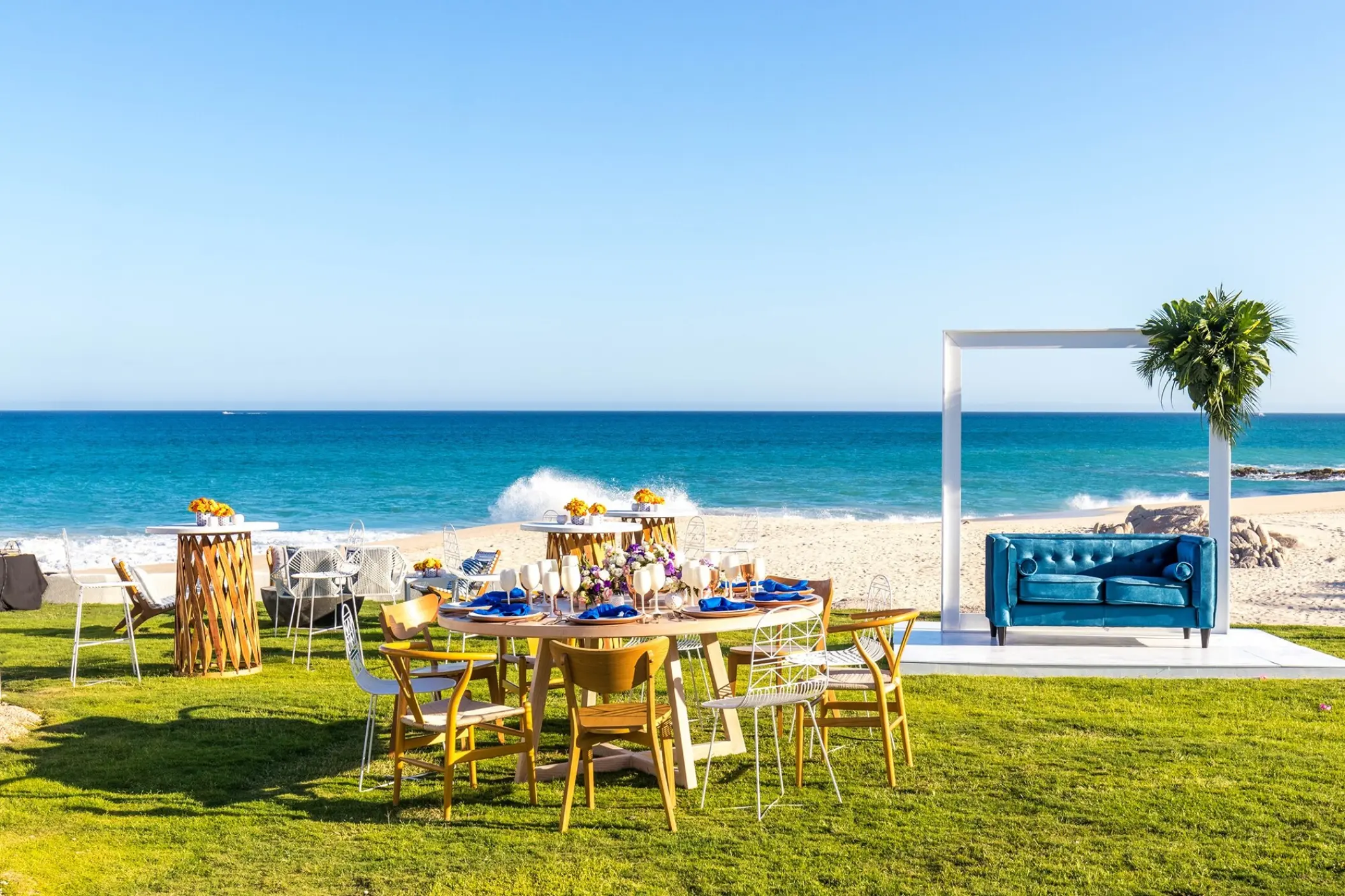 Beachfront wedding reception setup with wooden tables and blue sofa at Mar Del Cabo, Cabo San Lucas