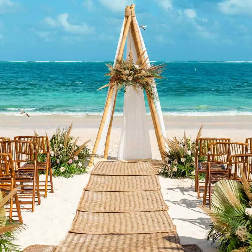 Beachfront wedding ceremony with a wooden triangular arch at The Fives Oceanfront, Riviera Maya