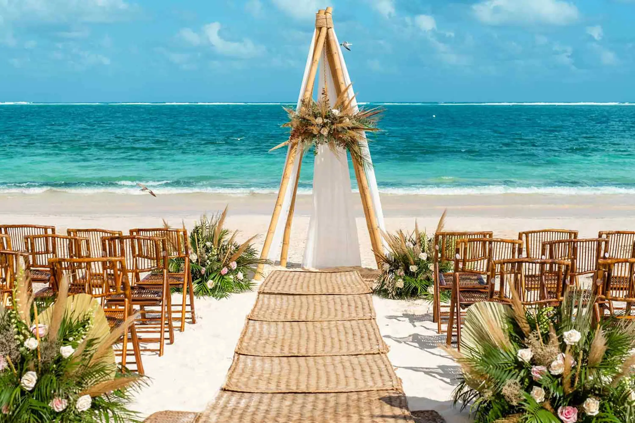 Beachfront wedding ceremony with a wooden triangular arch at The Fives Oceanfront, Riviera Maya