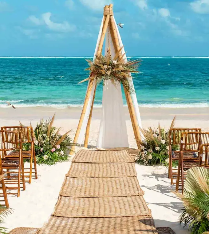 Beachfront wedding ceremony with a wooden triangular arch at The Fives Oceanfront, Riviera Maya
