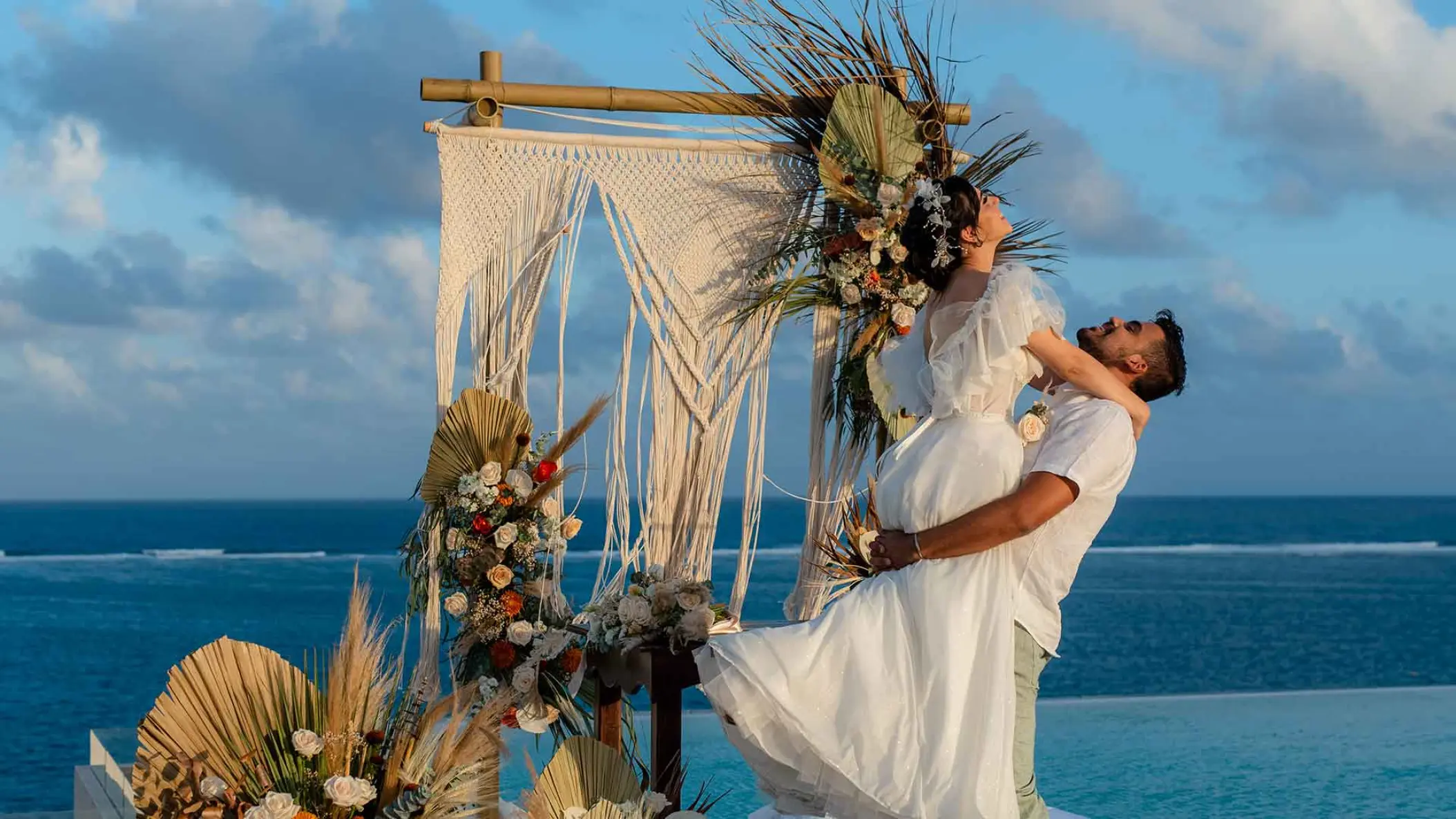 Groom lifting bride in front of a macrame arch at The Fives Oceanfront, Riviera Maya