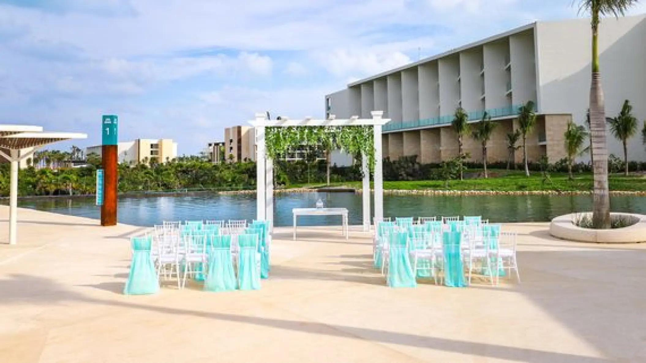 Waterfront wedding ceremony with turquoise chairs and white pergola at TRS Coral Hotel, Cancun