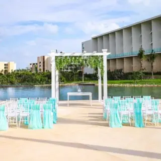 Waterfront wedding ceremony with turquoise chairs and white pergola at TRS Coral Hotel, Cancun