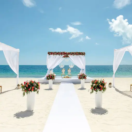Beachfront wedding ceremony setup with white floral arch and aisle at TRS Coral Hotel, Cancun