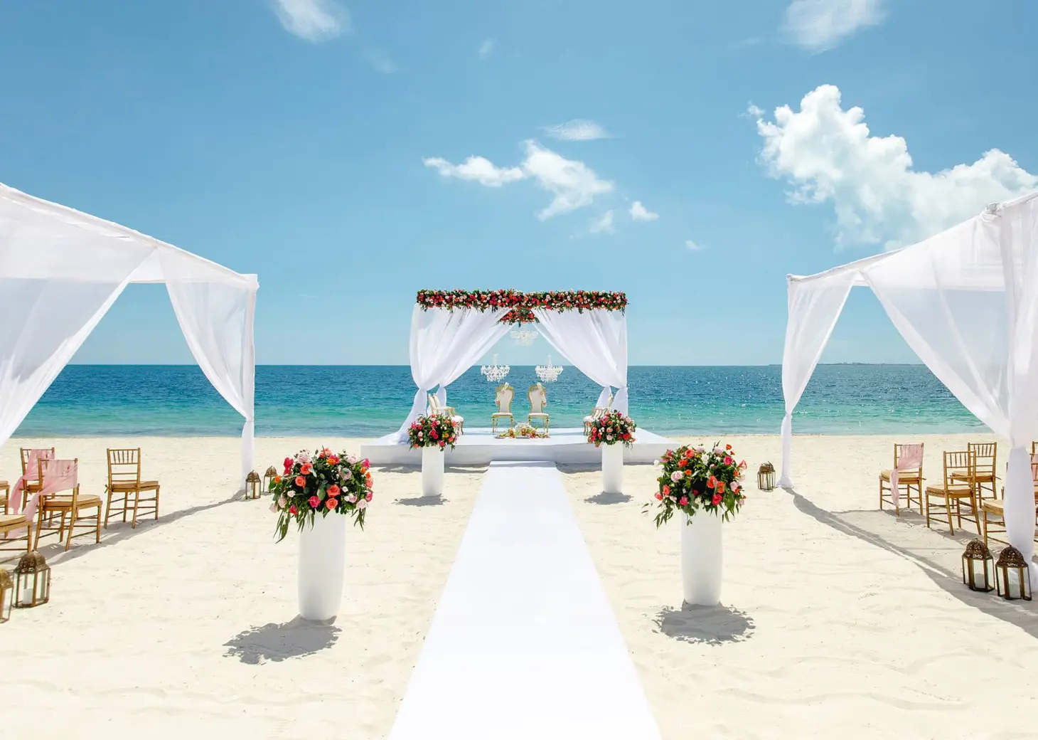 Beachfront wedding ceremony setup with white floral arch and aisle at TRS Coral Hotel, Cancun