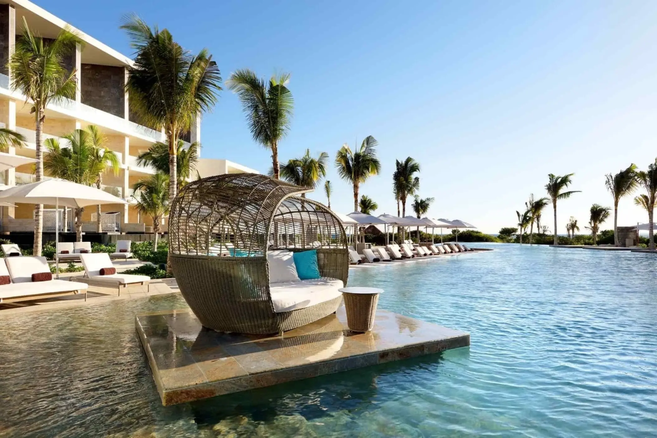 Main pool with wicker daybed and palm trees at TRS Coral Hotel, Cancun