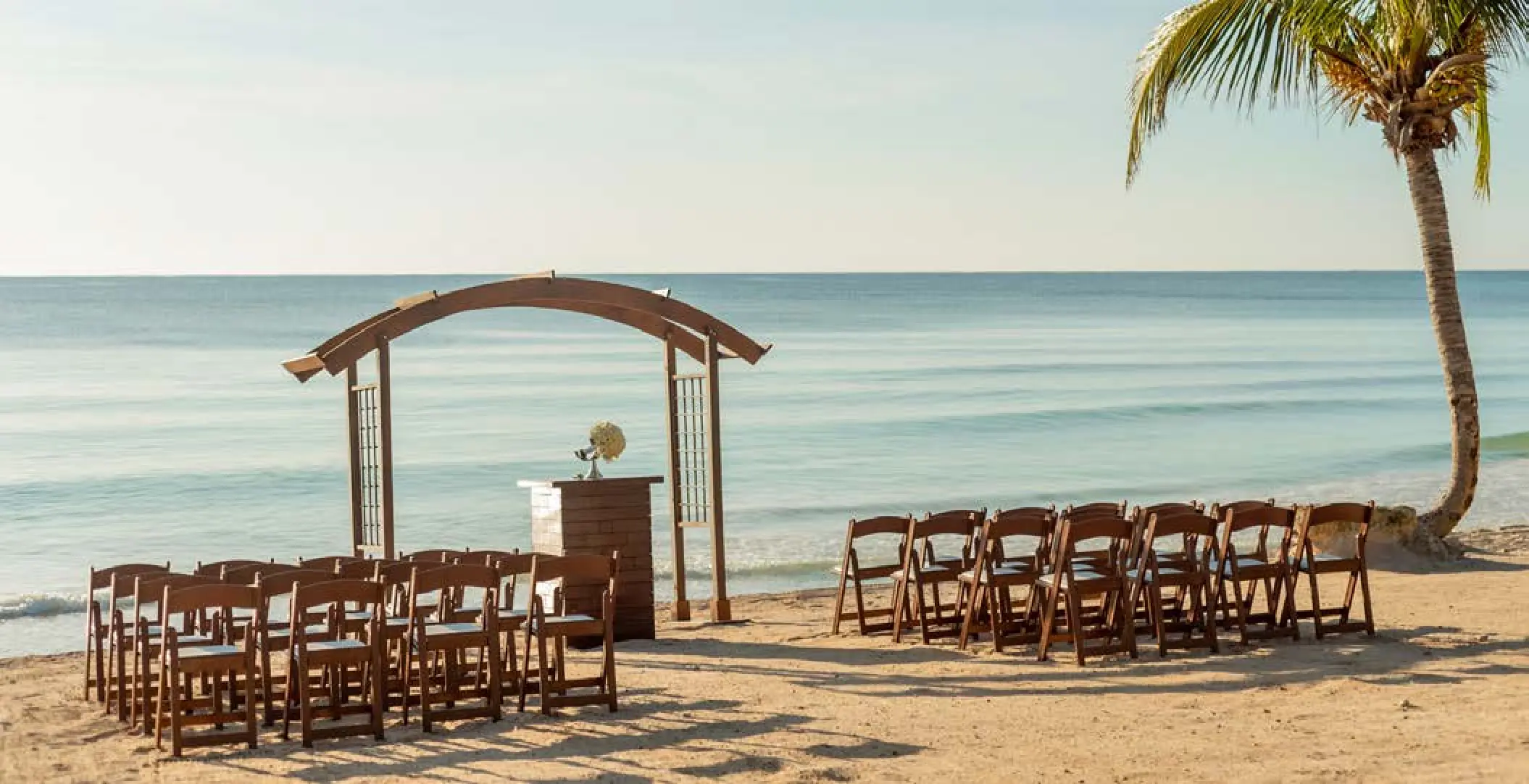 Beachfront wedding ceremony with wooden arch and chairs at UNICO 20°87°, Riviera Maya