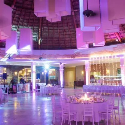 Wedding reception setup under a thatched palapa roof with purple lighting at Valentin Imperial, Riviera Maya