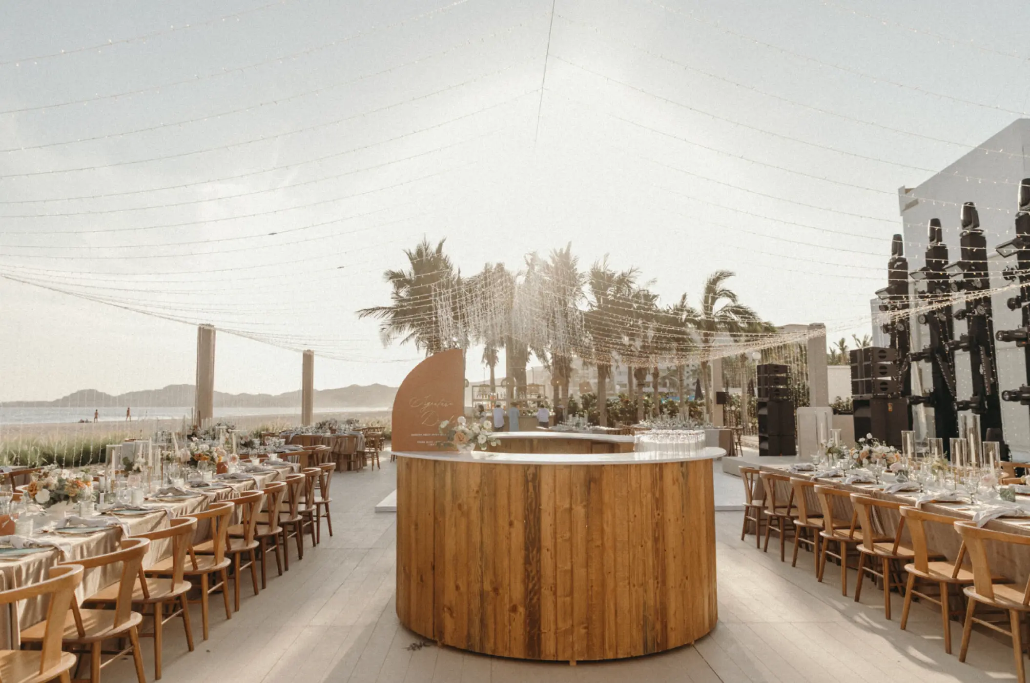 Beachfront wedding reception setup with wooden bar and string lights at Viceroy Los Cabos, Cabo San Lucas
