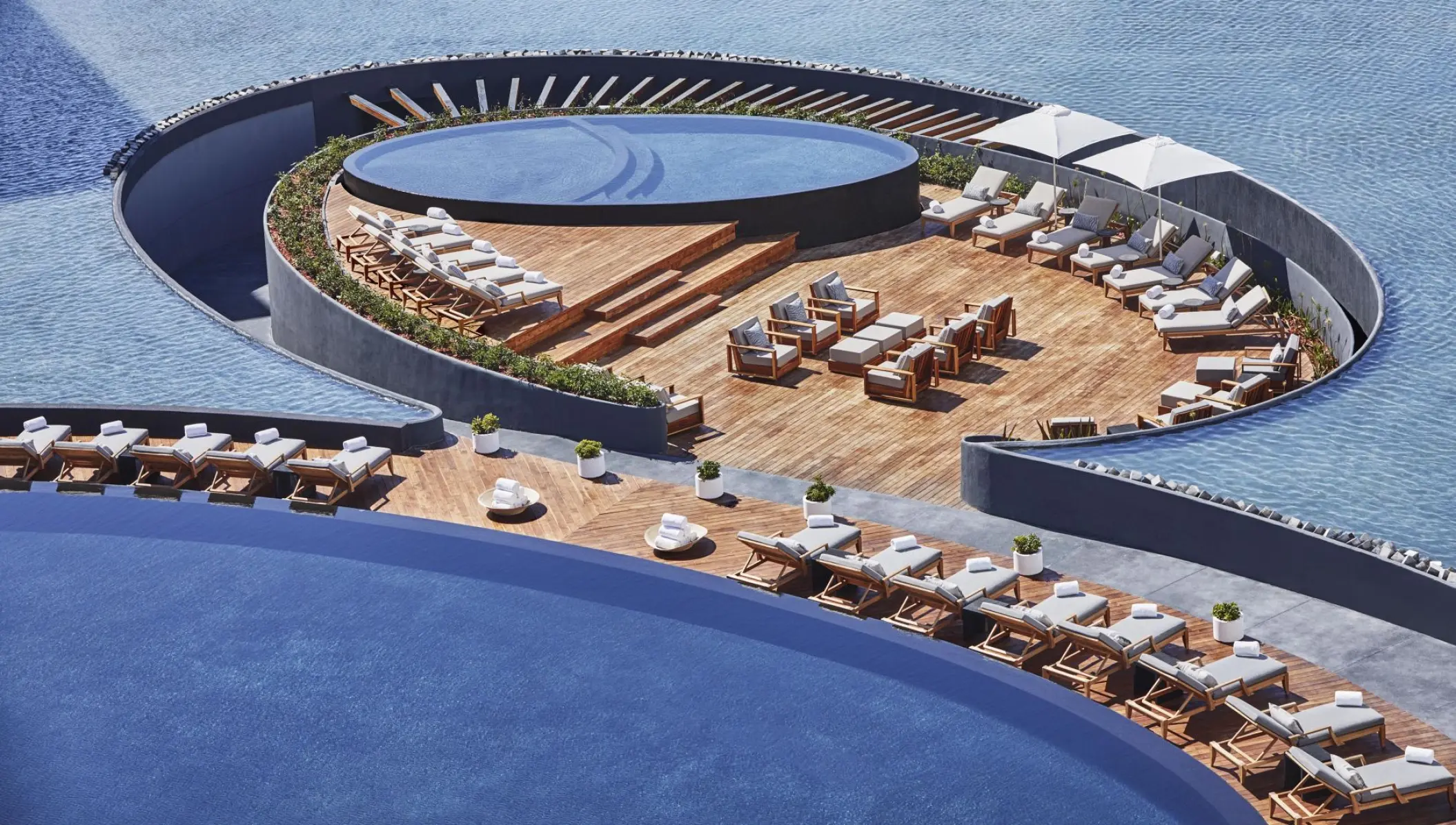 Aerial view of the modern circular pool and wooden deck with lounge chairs at Viceroy Los Cabos, Cabo San Lucas
