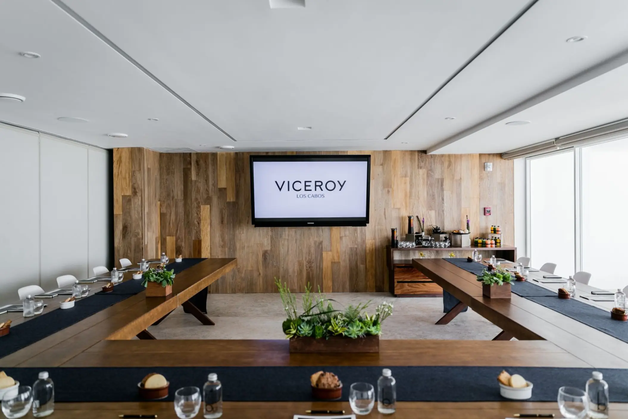 Indoor reception area with wooden tables and a branded television screen at Viceroy Los Cabos, Cabo San Lucas