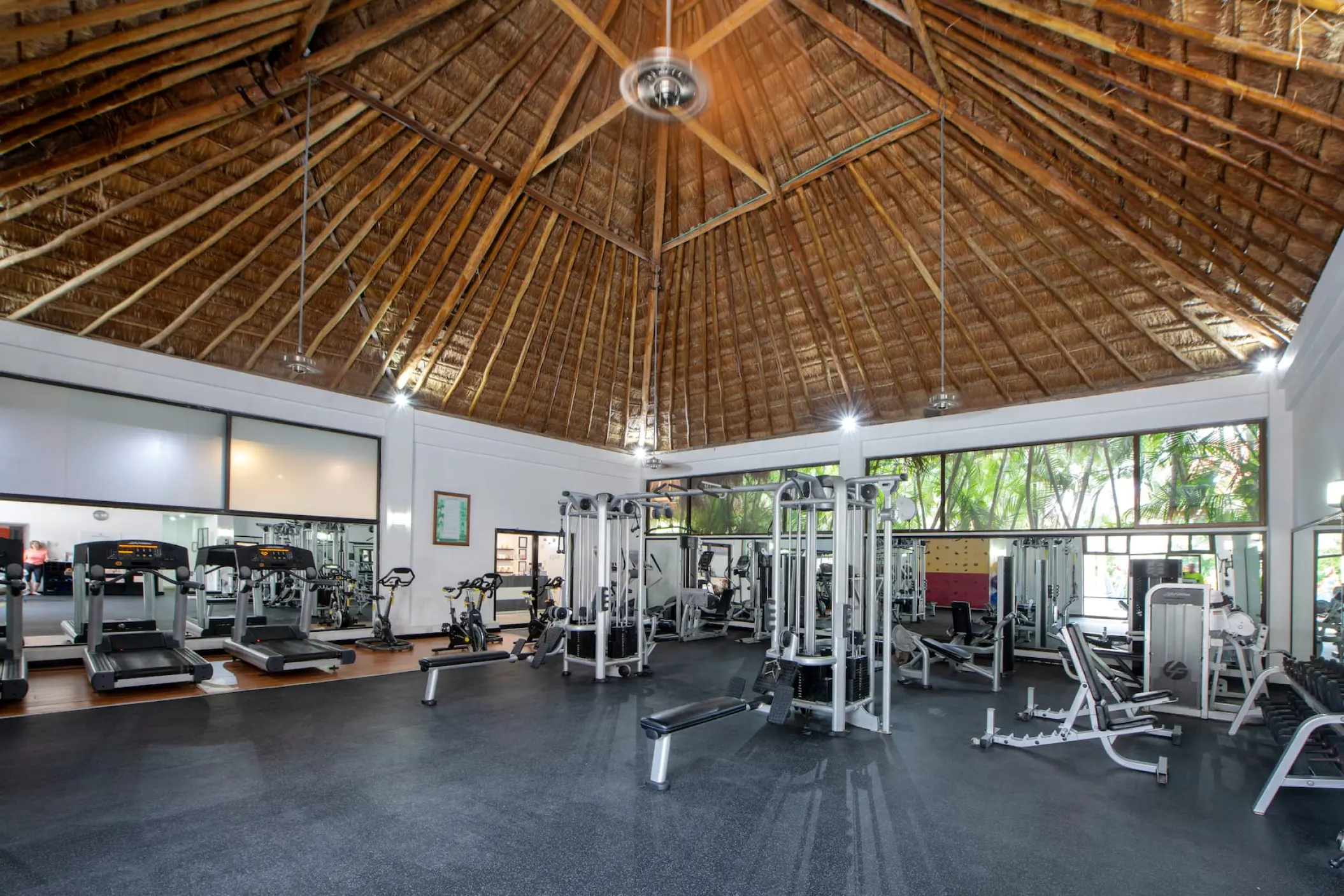 Fitness center with weight machines and treadmills under a thatched palapa roof at Viva Maya by Wyndham, Playa Del Carmen