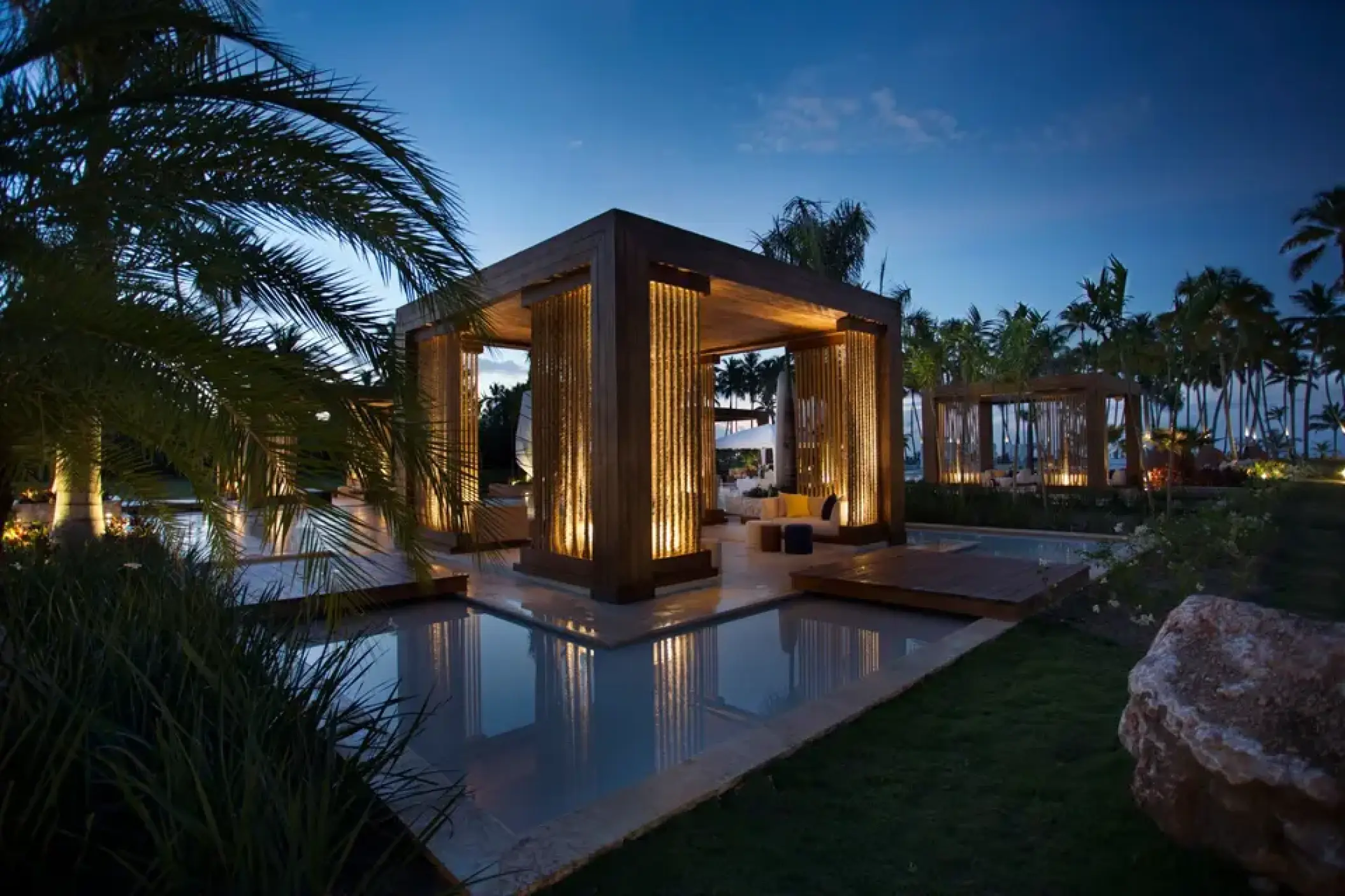 Lit wooden cabanas over water features at night at Viva V Samana, Samana