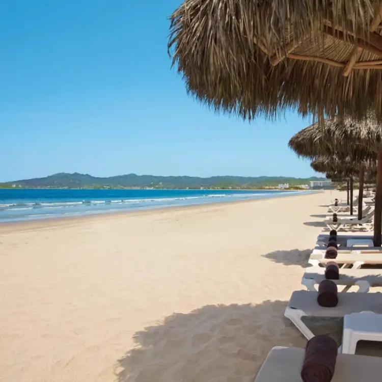 Palm leaf umbrellas and lounge chairs on the sand at Wyndham Alltra Riviera Nayarit, Puerto Vallarta