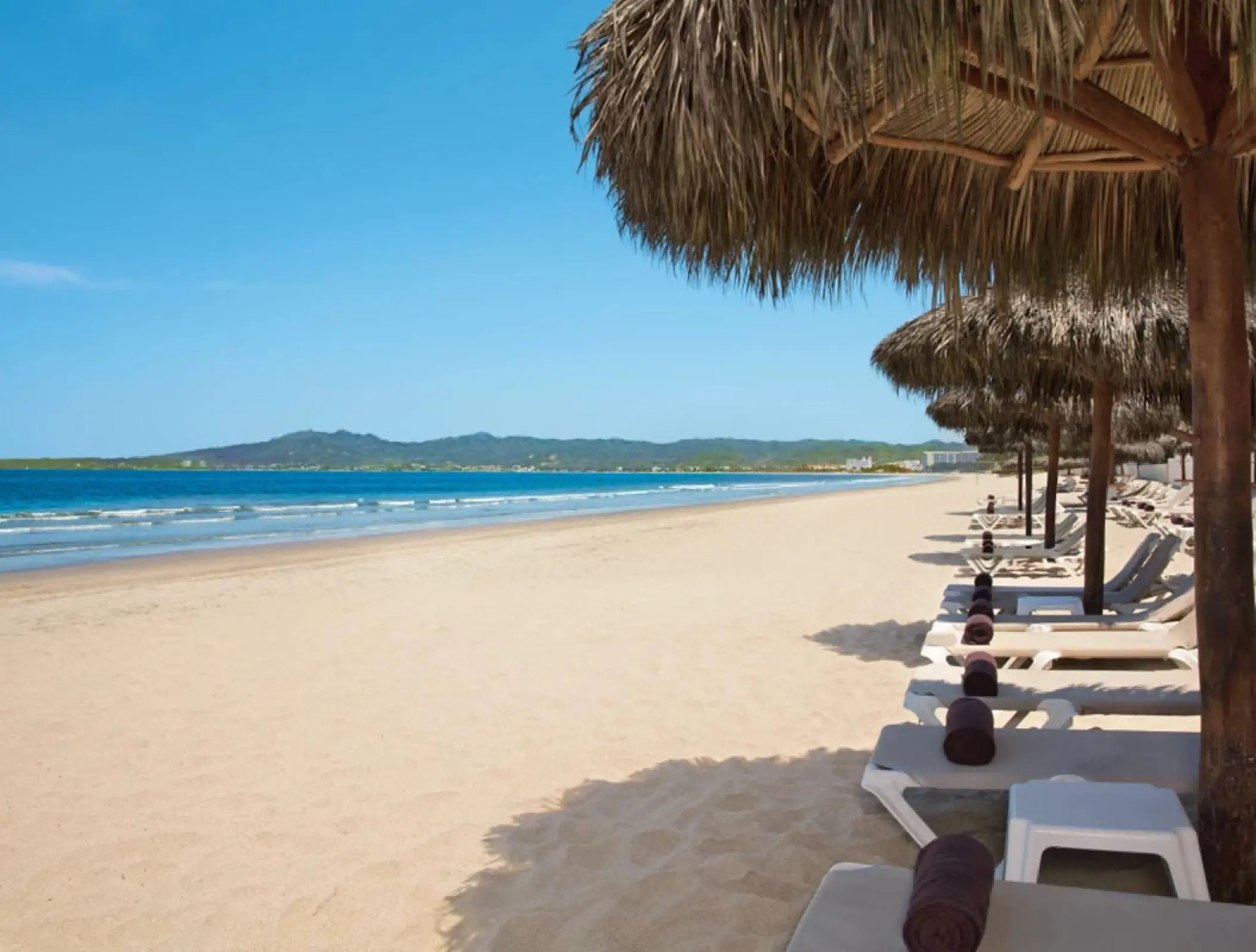 Palm leaf umbrellas and lounge chairs on the sand at Wyndham Alltra Riviera Nayarit, Puerto Vallarta