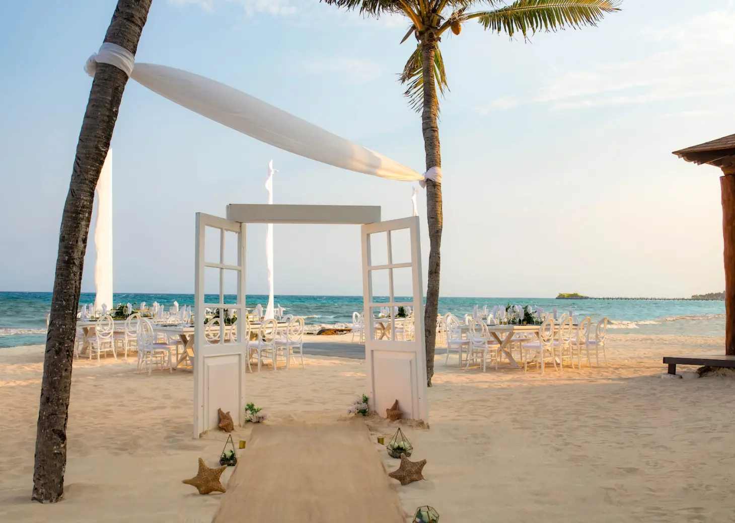 Beachfront wedding reception setup with white doors and palm trees at Wyndham Alltra, Playa Del Carmen