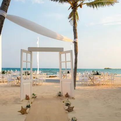 Beachfront wedding reception setup with white doors and palm trees at Wyndham Alltra, Playa Del Carmen