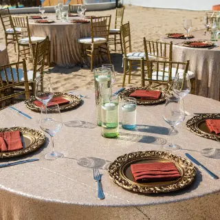 Wedding reception tables with gold linens and gold chairs on the beach at Wyndham Alltra Riviera Nayarit, Puerto Vallarta