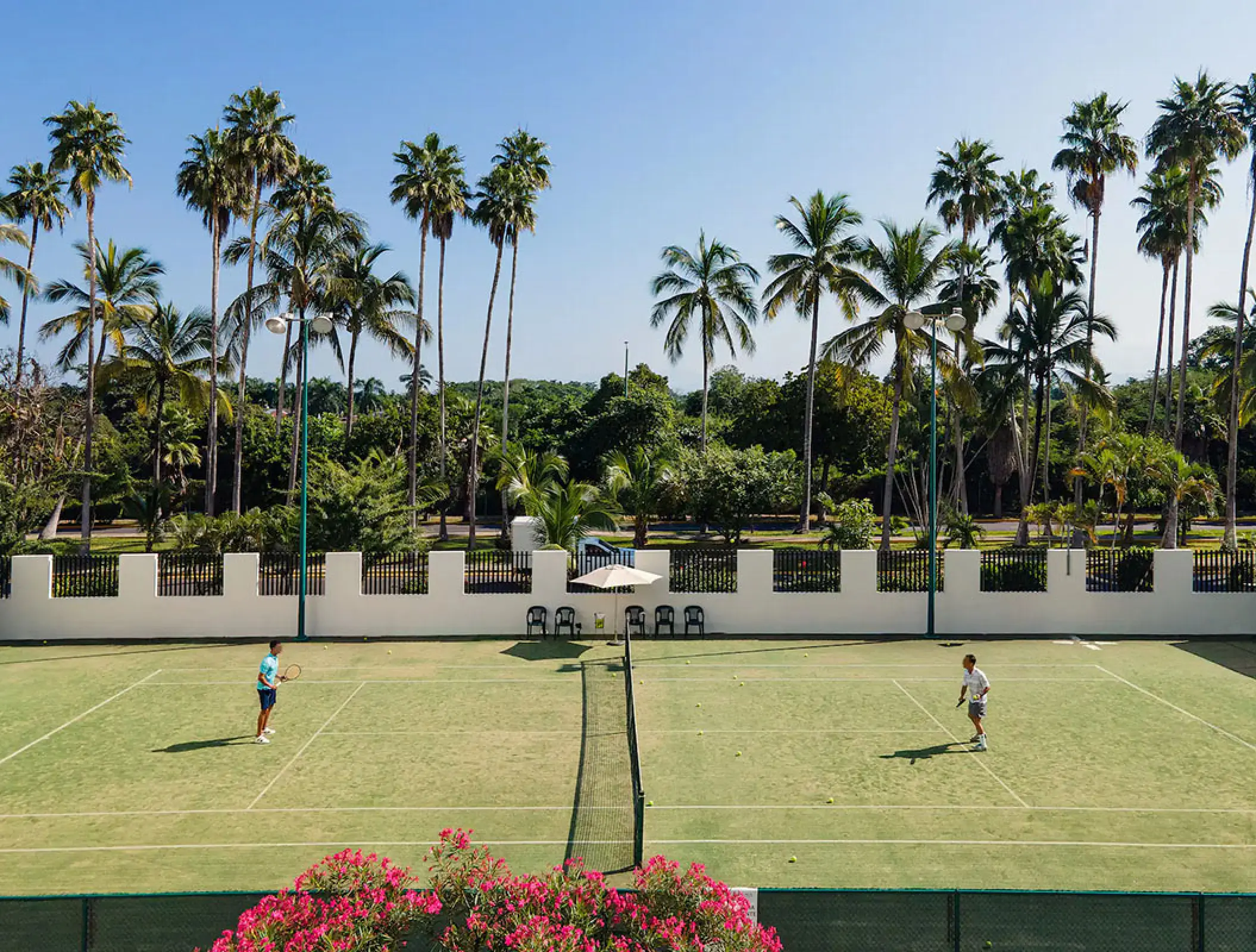 Two people playing tennis on a court lined with palm trees at Wyndham Alltra Riviera Nayarit, Puerto Vallarta