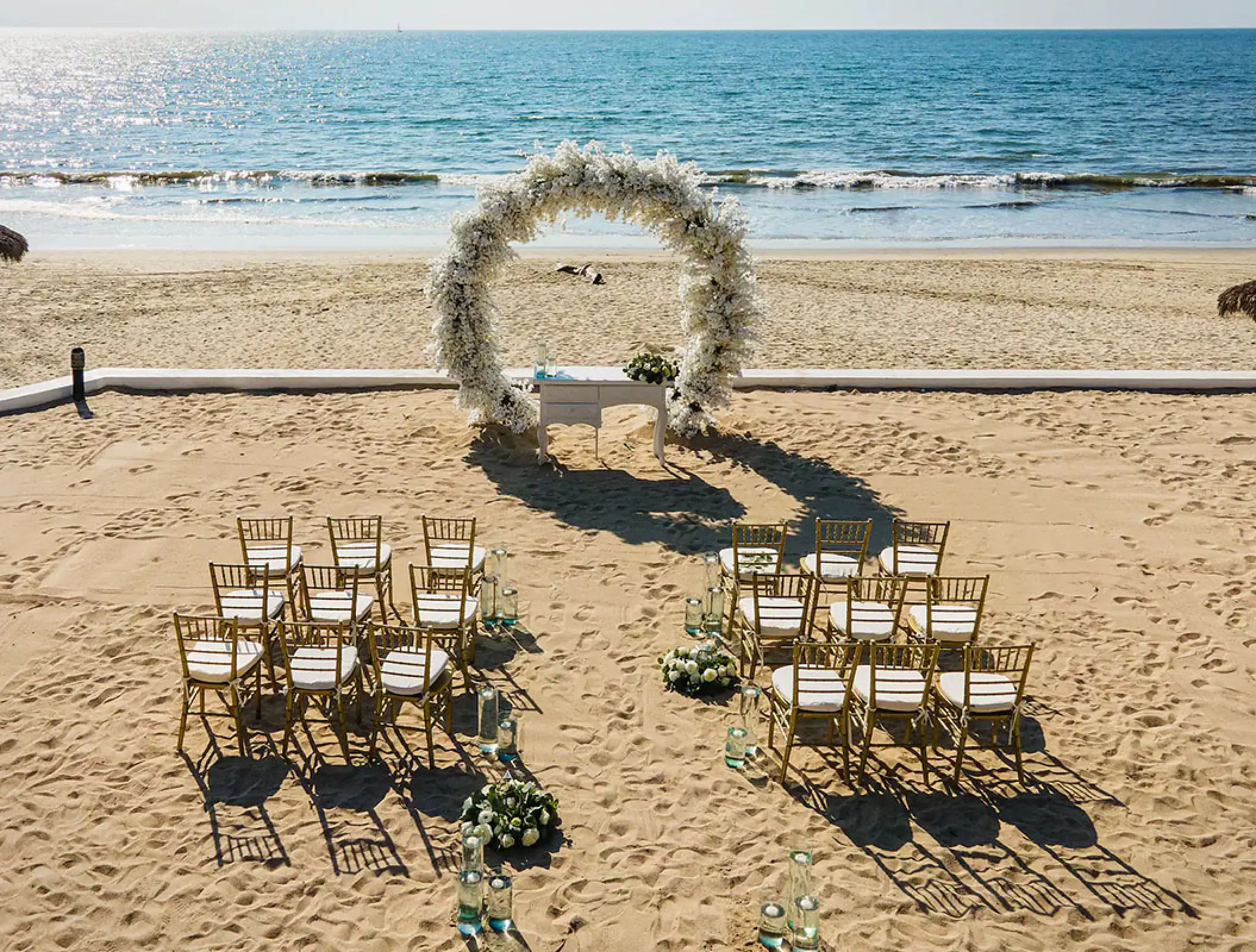 Beachfront wedding ceremony with white floral arch and gold chairs at Wyndham Alltra Riviera Nayarit, Puerto Vallarta