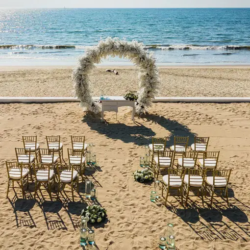Beachfront wedding ceremony with white floral arch and gold chairs at Wyndham Alltra Riviera Nayarit, Puerto Vallarta