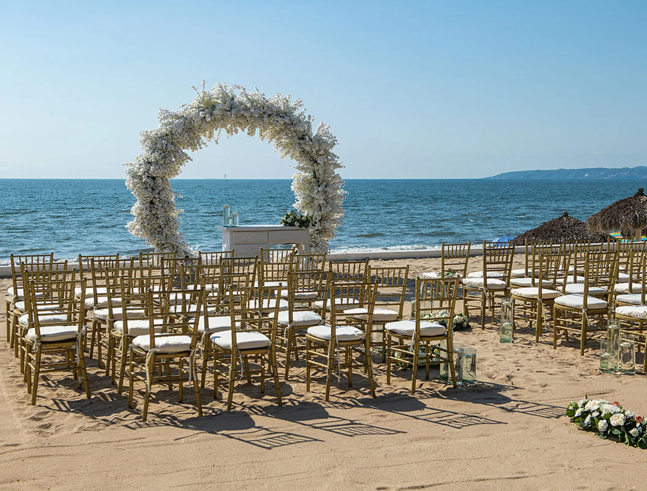 Beachfront wedding ceremony with white floral arch and gold chairs at Wyndham Alltra Riviera Nayarit, Puerto Vallarta