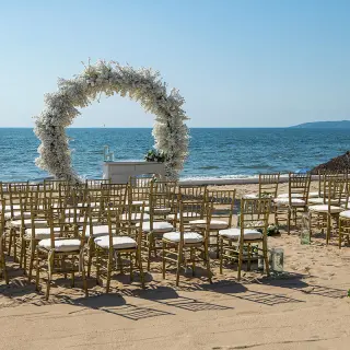 Beachfront wedding ceremony with white floral arch and gold chairs at Wyndham Alltra Riviera Nayarit, Puerto Vallarta