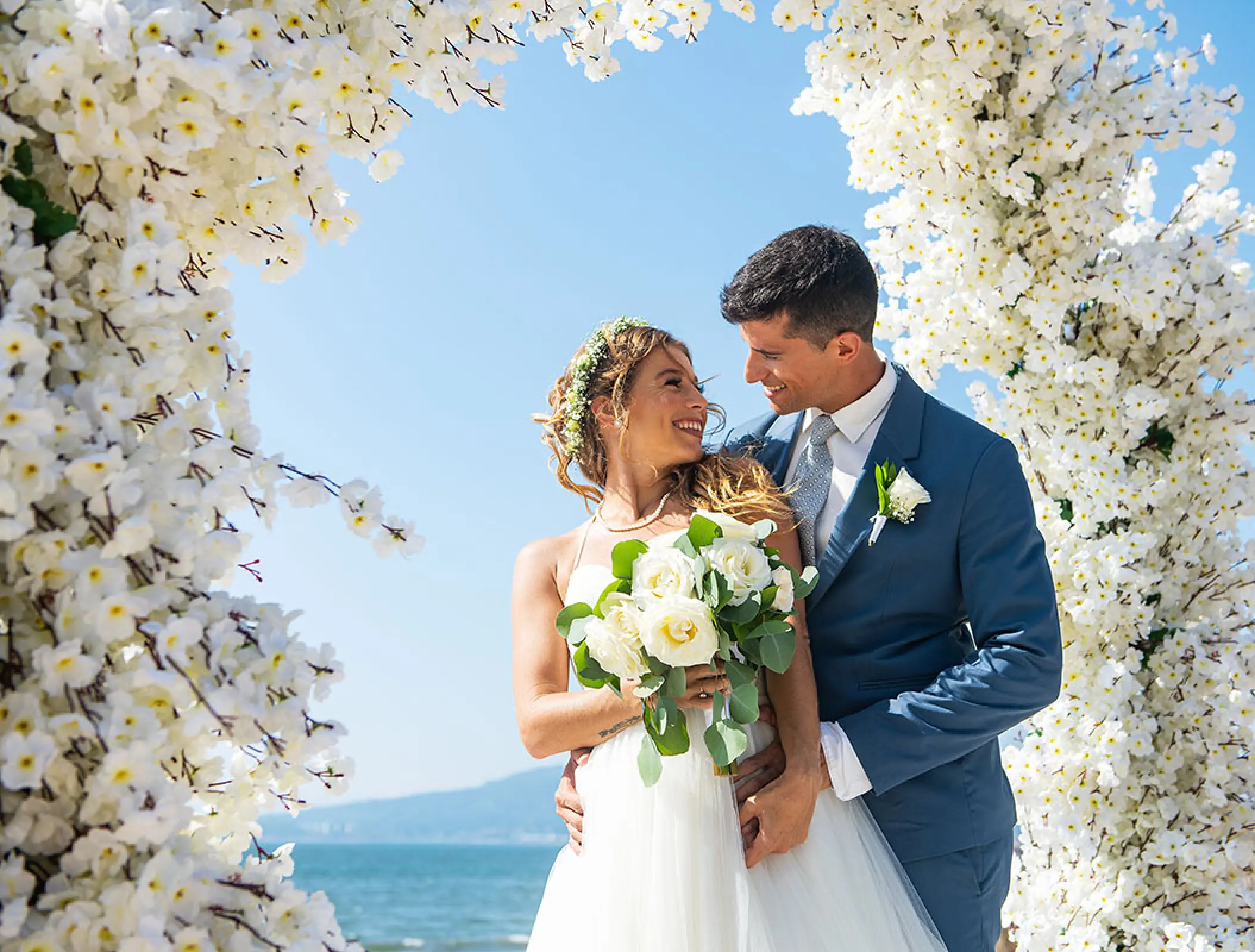The bride and groom smiling under a white floral arch at Wyndham Alltra Riviera Nayarit, Puerto Vallarta