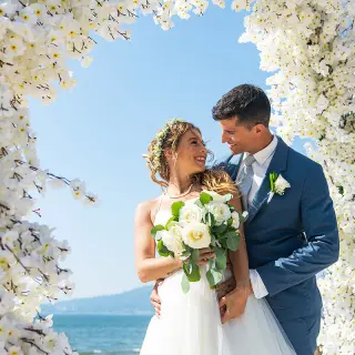 The bride and groom smiling under a white floral arch at Wyndham Alltra Riviera Nayarit, Puerto Vallarta