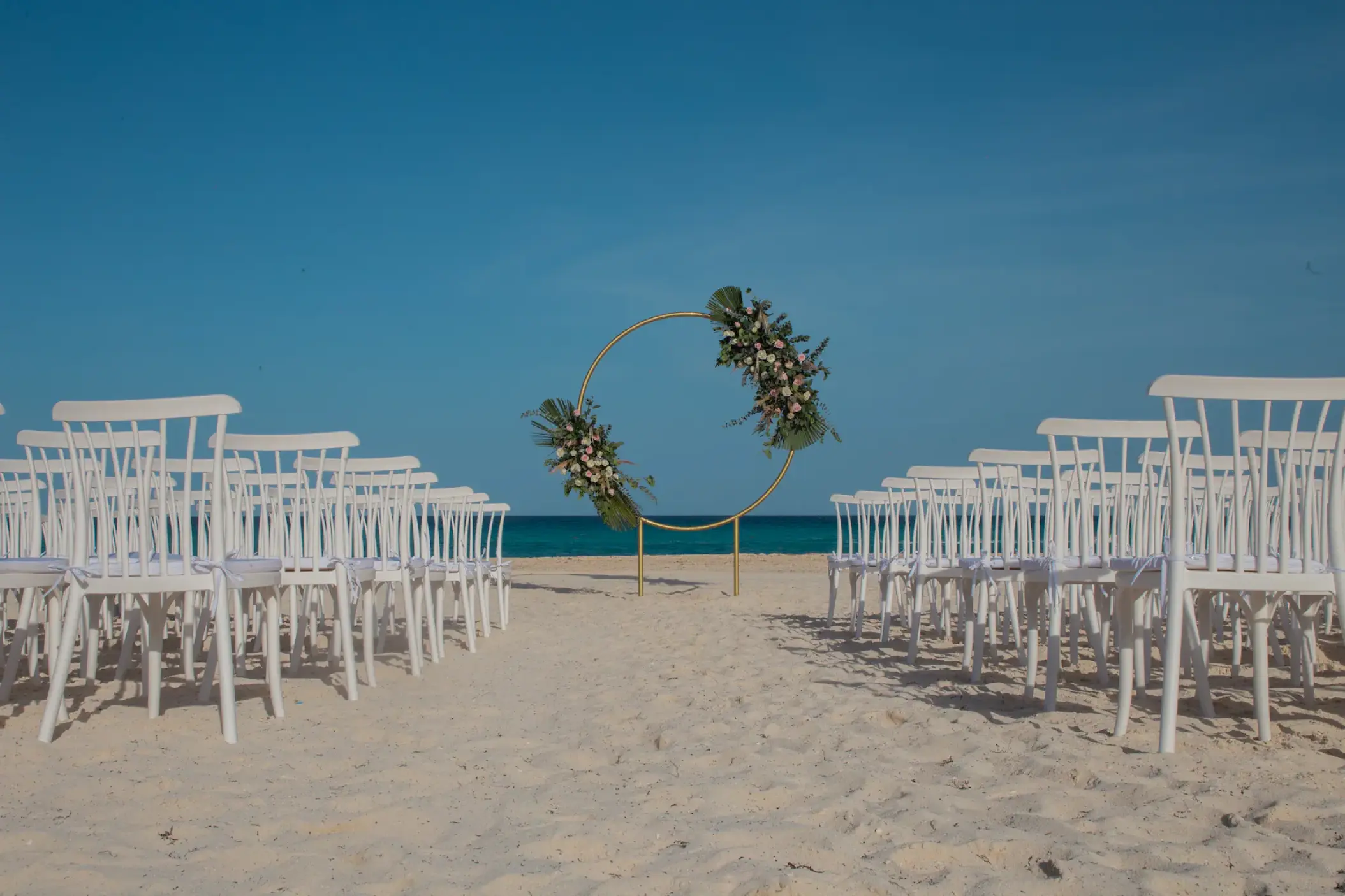 Beachfront wedding ceremony with circular floral arch and white chairs at Sunscape Cancun, Cancun