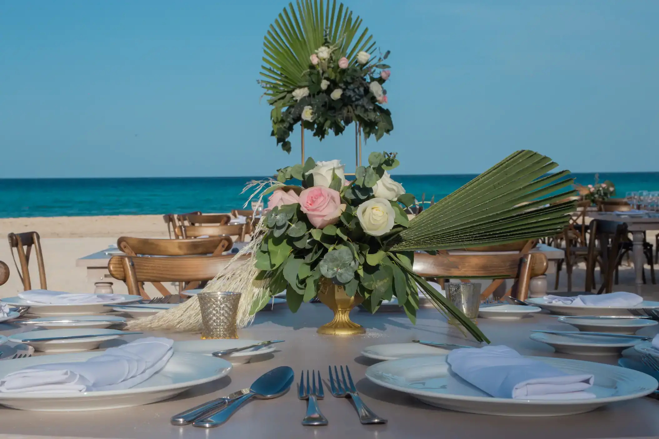 Beachfront wedding reception table with floral centerpieces and tropical leaves at Sunscape Cancun