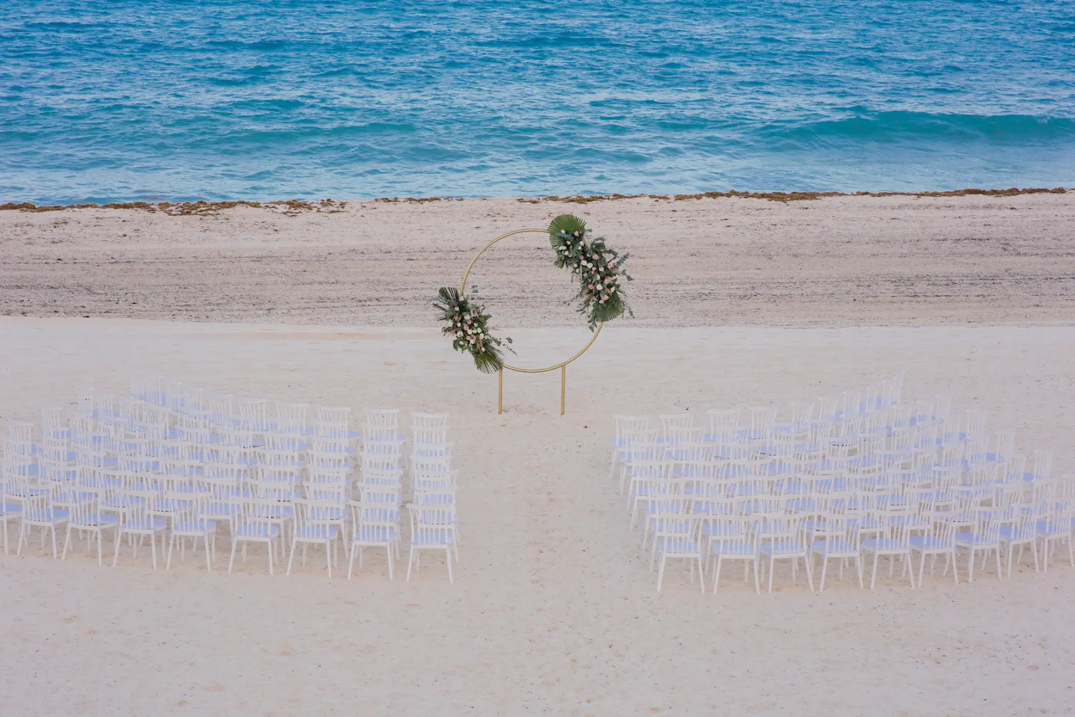 Beachfront wedding ceremony with white chairs and a circular floral arch at Sunscape Cancun, Cancun