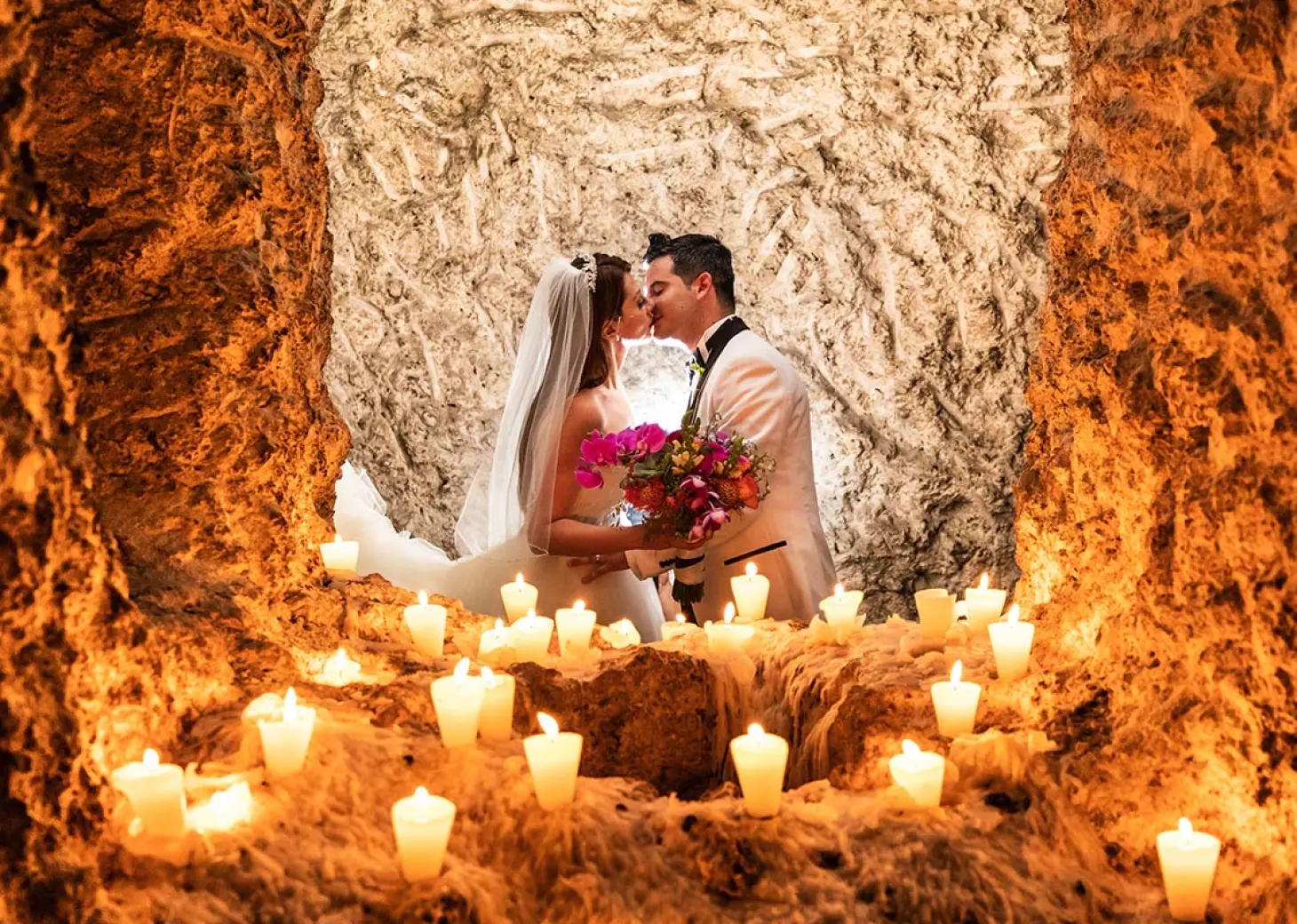 The bride and groom kissing in a candlelit cave at Hotel Xcaret Mexico, Riviera Maya