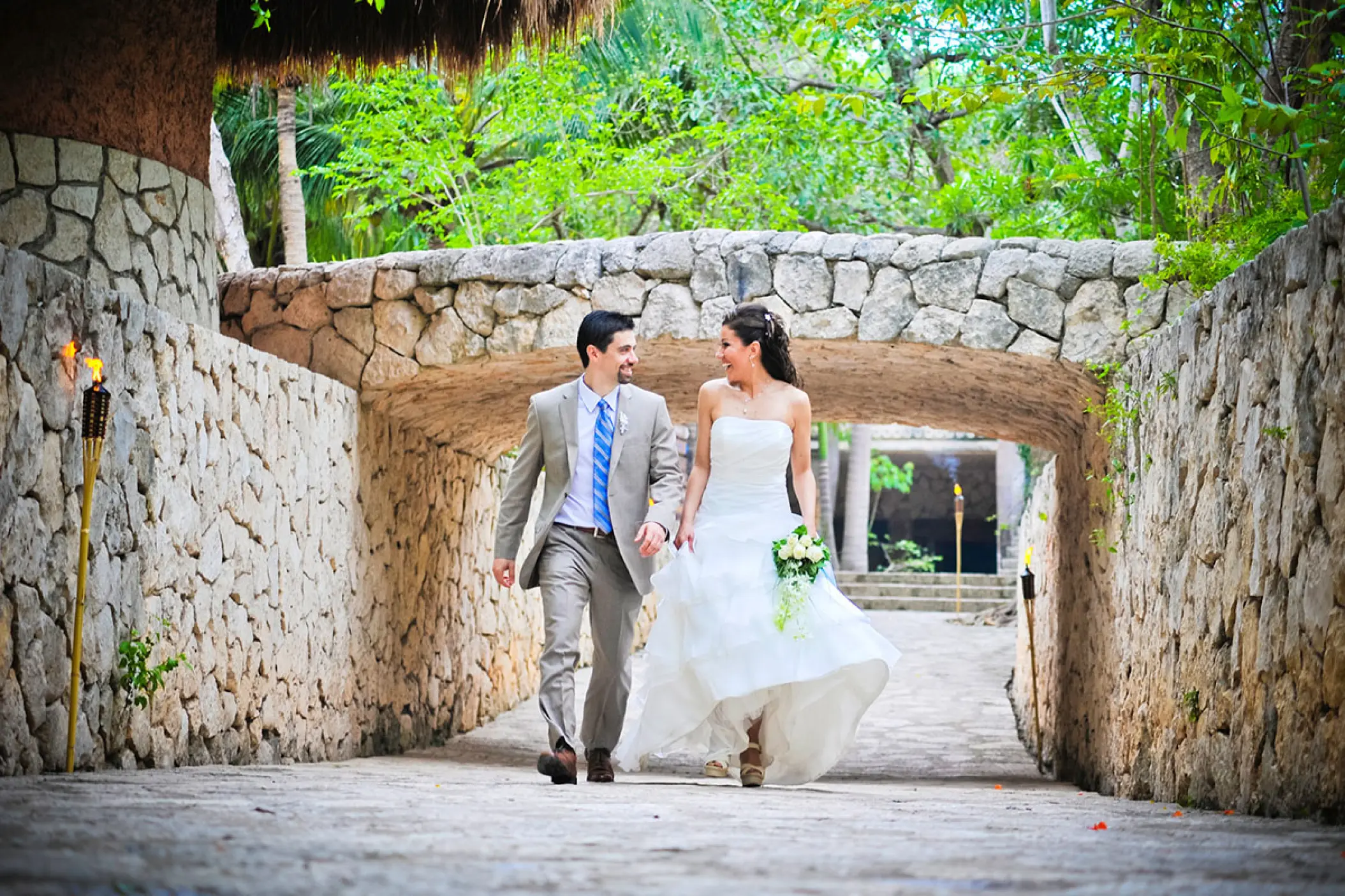 Newlyweds walking and smiling through a stone tunnel at Hotel Xcaret Mexico, Riviera Maya