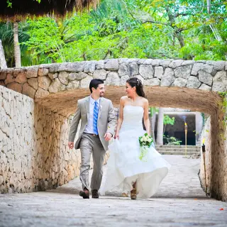 Newlyweds walking and smiling through a stone tunnel at Hotel Xcaret Mexico, Riviera Maya