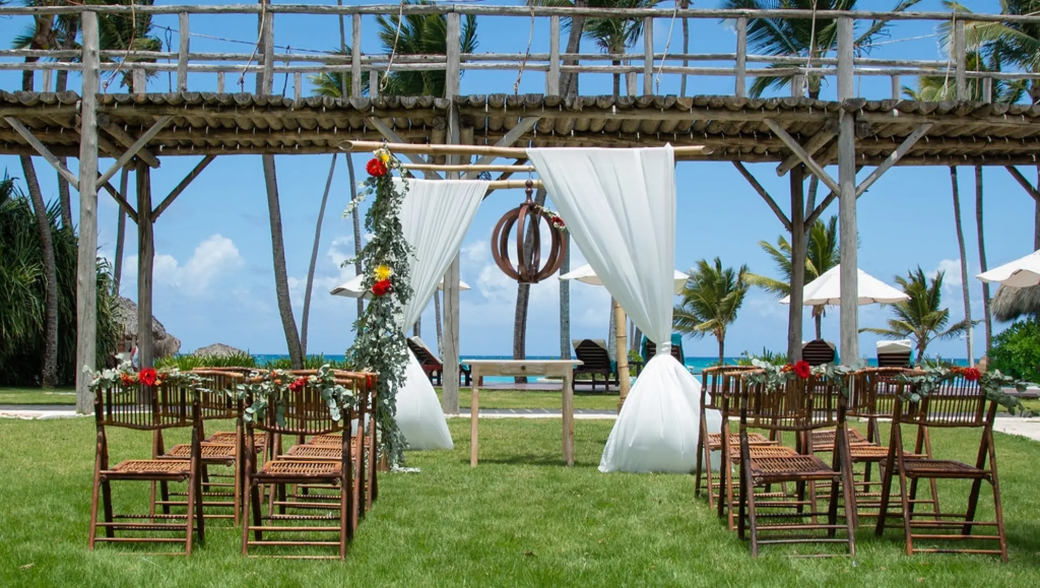 Garden wedding ceremony setup with wooden chairs and white fabric arch at Zoetry Agua, Punta Cana