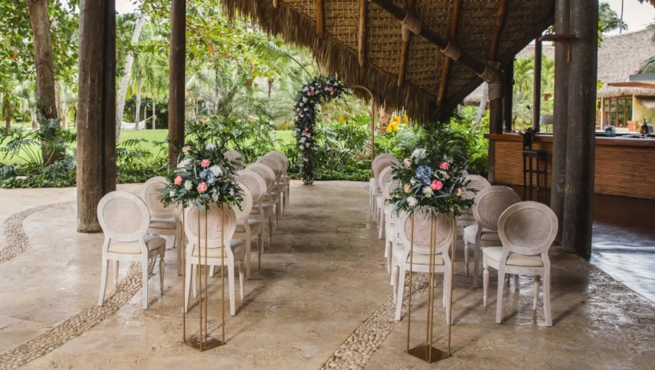 Sheltered terrace wedding ceremony with floral stands and round-back chairs at Zoetry Agua, Punta Cana